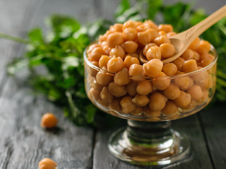 Glass bowl filled with boiled chickpeas with wooden spoon.