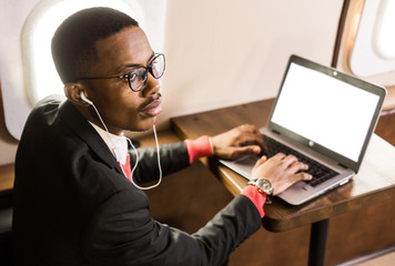 Attractive and successful African American businessman with glasses working on a laptop while sitting in the chair of his private jet