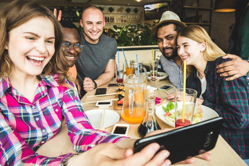 Group of young cheerful friends are sitting in a cafe, eating, drinking drinks. Friends take selfies and take pictures.