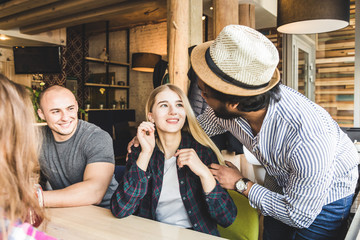 a group of young cheerful friends are sitting in a cafe, eating, drinking drinks, take selfies and take pictures. meeting, handshake and hugs