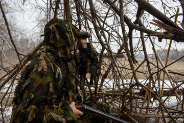 A hunter in a hut from the branches looks out for prey with binoculars.