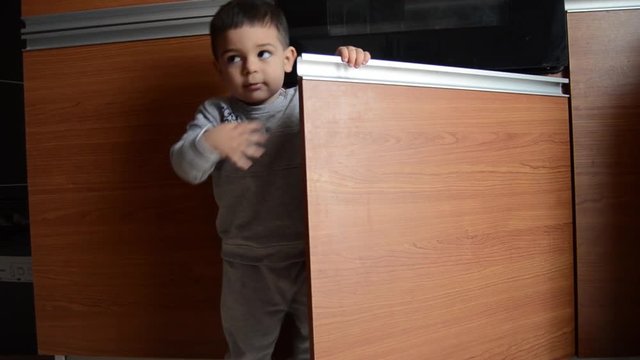 Cute two years old boy hiding in the kitchen cupboard under the built-in owen, hide and seak