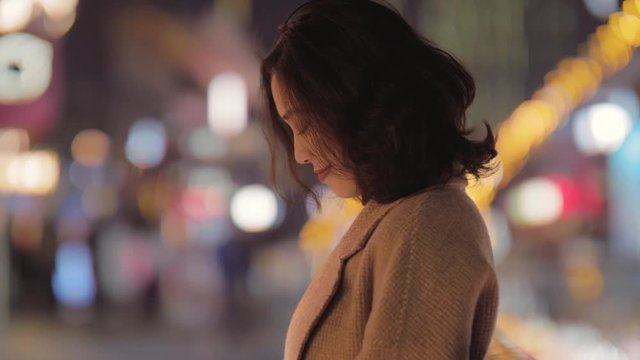 A Chinese lady, bowing her head and fiddling with her mobile phone in the street,the whole person looked very gentle, with a faint smile on the corners of her mouth,