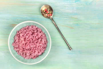 Obraz na płótnie Canvas A bowl of pink Himalayan sea salt with a pepper mix, shot from the top on a teal blue background with copy space