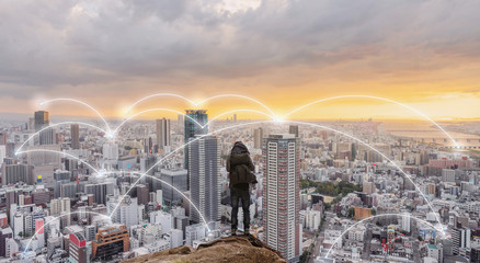 Smart city, wireless network and internet system in the city. Businessman standing on mountain peak with cityscape in sunset