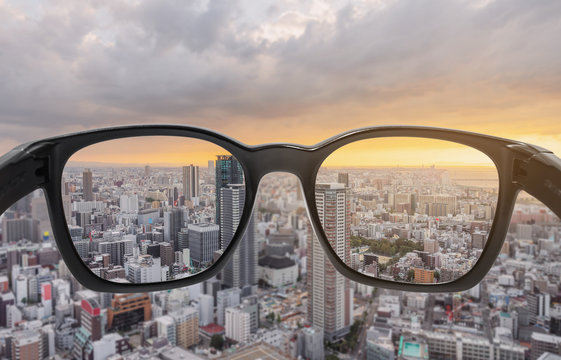 Looking through eyeglasses to city sunset view, focused on lens with blurry background	