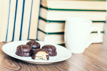 Stack of books, cup of coffee and chocolate cookies white plate.