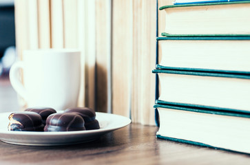 Stack of books, cup of coffee and chocolate cookies white plate.