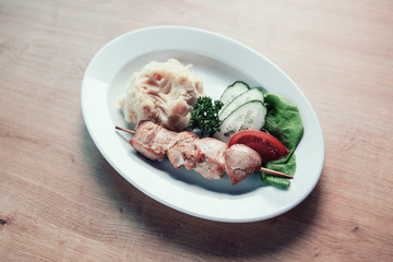 pork kebab ,mashed potatoes and slices of fresh vegetables in a plate
