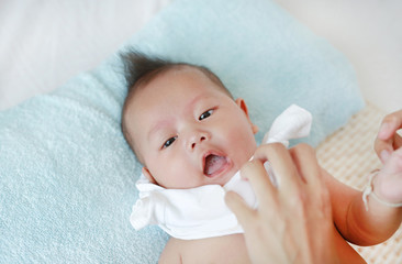 Cute asian infant baby boy lying on bed and mother while put on some clothes to her baby after bath.