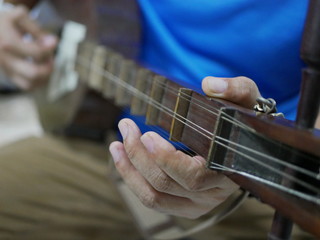 Hands of a musician playing Seung, plucked lute from the Lanna region of northern Thailand, made of hardwood - Traditional Thai musical instrument