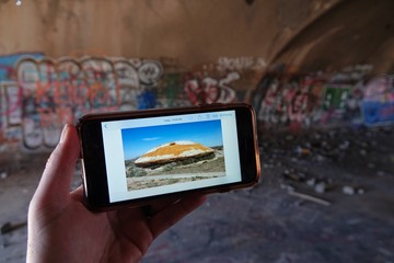 mobile phone in hand mobile phonrshowing the exterior of a graffiti filled abandoned building.