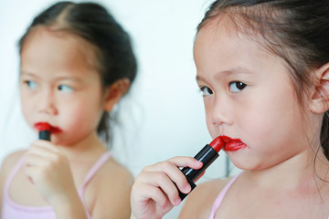 Adorable little Asian child girl trying mother's lipstick near a mirror.