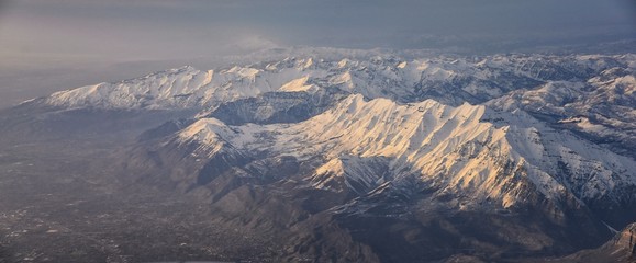 Aerial view from airplane of the Wasatch Front Rocky Mountain Range with snow capped peaks in winter including urban cities of Provo, Farmington Bountiful, Orem and Salt Lake City. Utah. United States