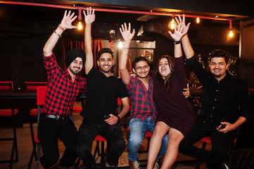 Group of indian friends sitting at lounge bar, having fun and rest. Hands up.