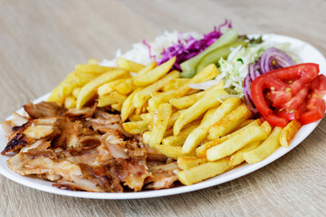 Chiken Doner Kebab on the plate with french fries, tomatoes, onion, pickles and salad on a wooden background. Grilled chicken meat with vegetables.