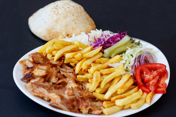 Chiken Doner Kebab on the plate with bread, french fries, tomatoes, onion, pickles and salad on a...