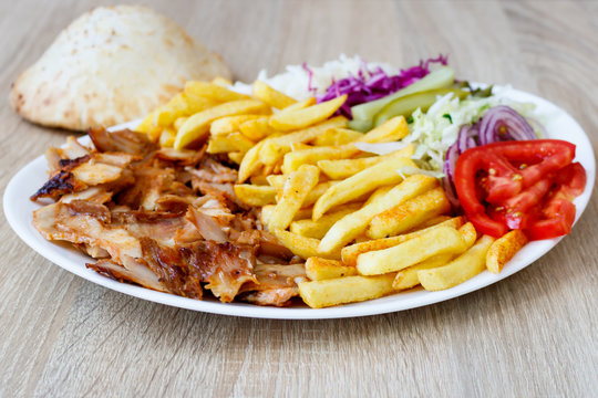 Chiken Doner Kebab on the plate with bread, french fries, tomatoes, onion, pickles and salad on a wooden background. Grilled chicken meat with vegetables.