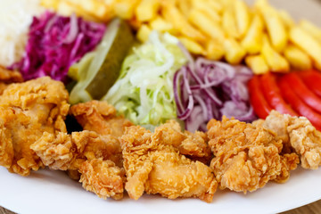 Chicken wings on the plate with french fries, tomatoes, onion, pickles and cabbage salad on a wooden background.