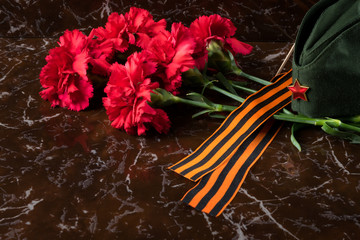 Red carnations with orange St. George ribbon lying on the Victory Day on a brown plate in memory of the soldiers