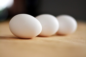 Three white raw eggs lie on the beige surface of the table in the kitchen and are reflected. Horizontal photo, large eggs. Preparing for Easter. Easter Ingredients