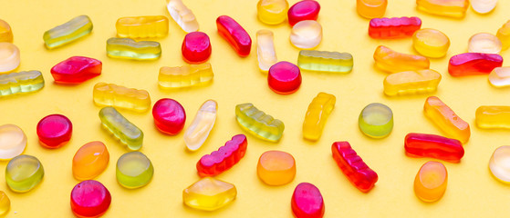 Colorful jelly candies assortment on yellow color background, closeup view