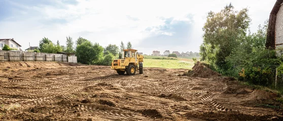Fotobehang large yellow wheel loader aligns a piece of land for a new building, wih copy space, banner © Hanna