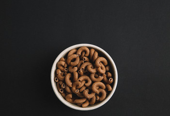 Whole grain elbow macaroni on dark background, top view, free space for text