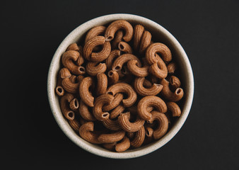 Whole grain elbow macaroni on dark background, top view