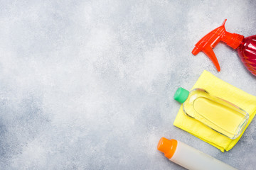 Bottles with detergents, brushes and sponges on concrete background. Colorful cleaning products. Home cleaning concept. Top view, copy space.