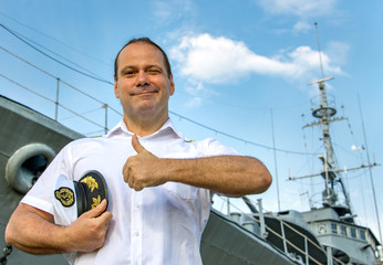 Captain standing in dock before warship and  shows thumb up. A sailor officer in white uniform...