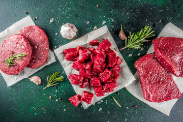 Various raw beef meat with spices and herbs, dark concrete background copy space
