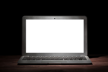 One silver modern laptop with empty white screen on wooden table in a dark room on black...