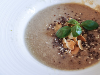 Close up of a brown creamy mushroom soup with chia seeds, white sesame, sliced almond and basil on top. Healthy food concept.