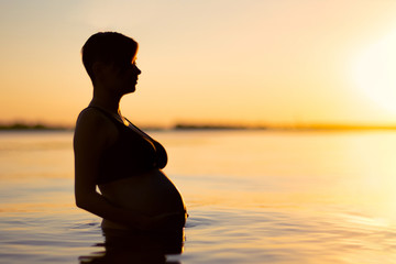 Fototapeta premium Silhouette of a pregnant woman in the water during sunset