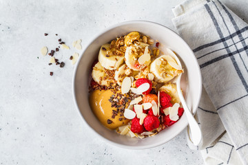 Granola with berries, banana, peanut butter and chocolate in a white bowl.