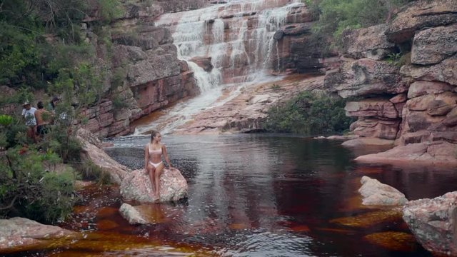 Slow Motion: Woman Sitting On Rock Next To Stream At Bottom Of Waterfall in Chapada, Brazil