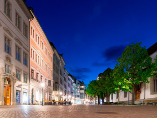 Schaffhausen, SH / Switzerland - 22 April, 2019: the Kirchhofplatz square on a spring evening with people eating out and bright city light colors under a blue sky