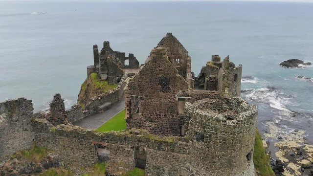 Descending drone capturing the Northern Atlantic Ocean behind the Dunluce Castle ruins on a cloudy day