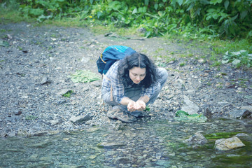Tourist woman drinking water from a creek