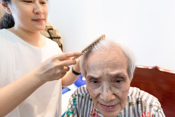 Asian young woman combing hair of senior woman in home,care assistant combing hair of elderly woman...