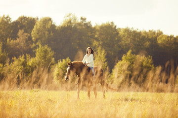 Naklejka premium Young girl goes sorrel horse riding in field
