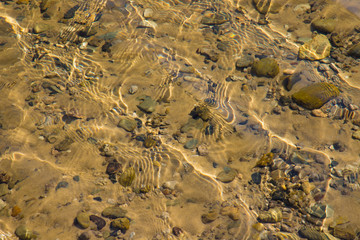 Transparent water surface with ripples through which the sandy bottom with pebbles is visible