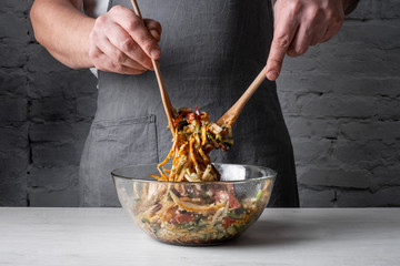 Chef hands cooking asian dish - mix salad with sliced beef and vegetables assorted on cuisine...