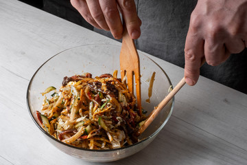 Chef hands cooking asian dish - mix salad with sliced beef and vegetables assorted on cuisine background.