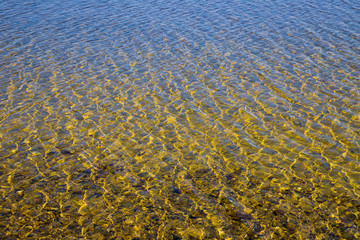 Transparent water surface with ripples through which the sandy bottom with pebbles is visible