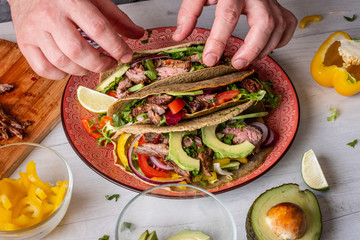 Mexican tacos with beef in sauce and vegetables salsa with ingredient cooking on background.