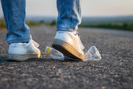 Legs crush plastic bottle on the road. Environmental conservation