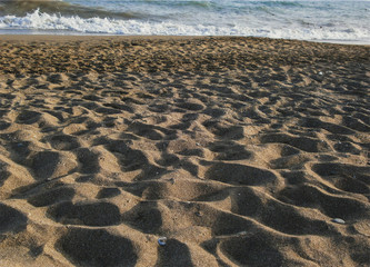 A beach of yellow sand, ashore sea wave runs up. On the sand there are grooves from the feet of tourists.