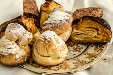 Pieces of various cakes with eclairs and traditional Armenian cookies "Gata" and baklava from puff pastry on a vintage porcelain plate